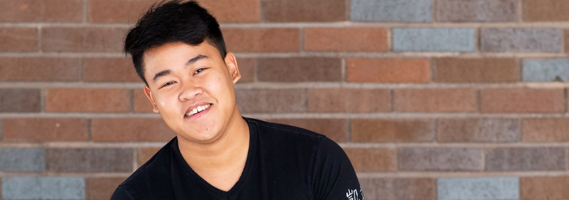 young man sitting in front of rock wall smiling at camera