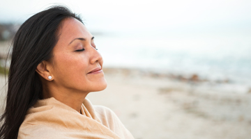 Woman peacefully standing on beach with eyes closed