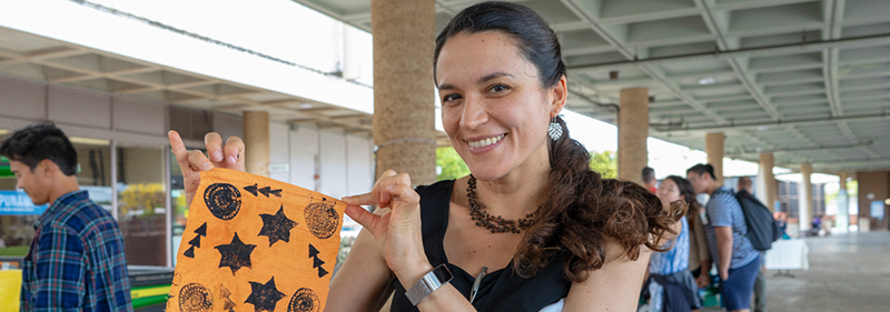 woman holding up small fabric artwork and smiling at camera