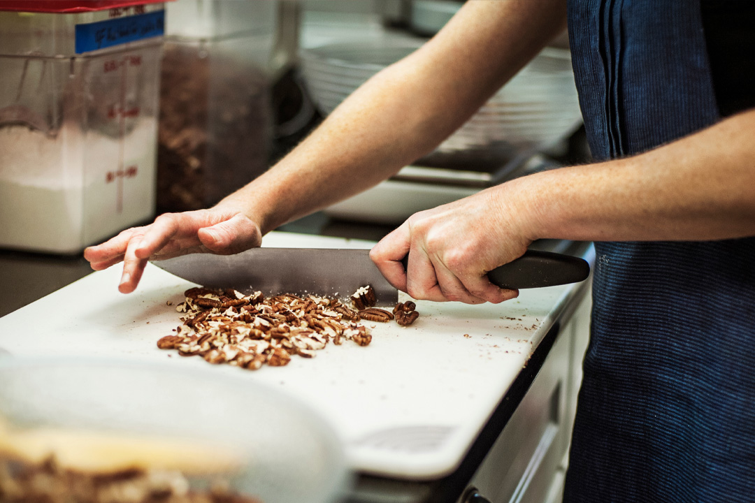Closeup of chef in kitchen chopping pecans