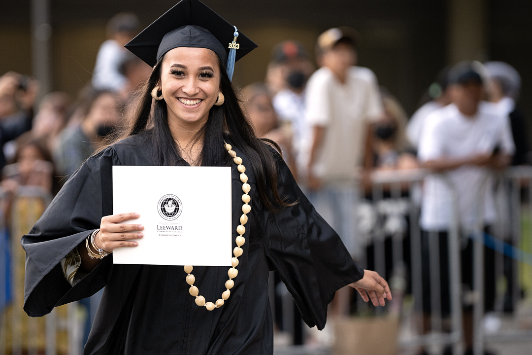 Leeward graduate walking toward tent during ceremony, holding her mock diploma