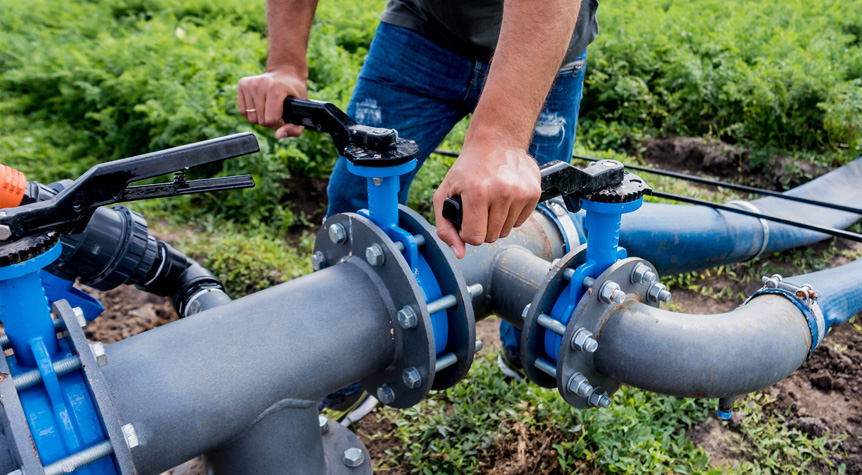 person adjusting valves on irrigation piping